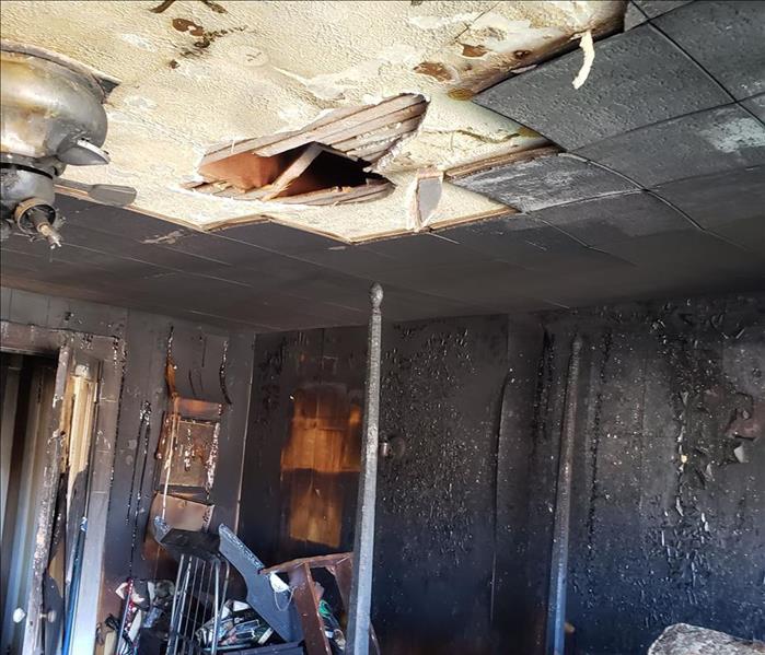 Room with missing ceiling tiles covered in soot from fire damage